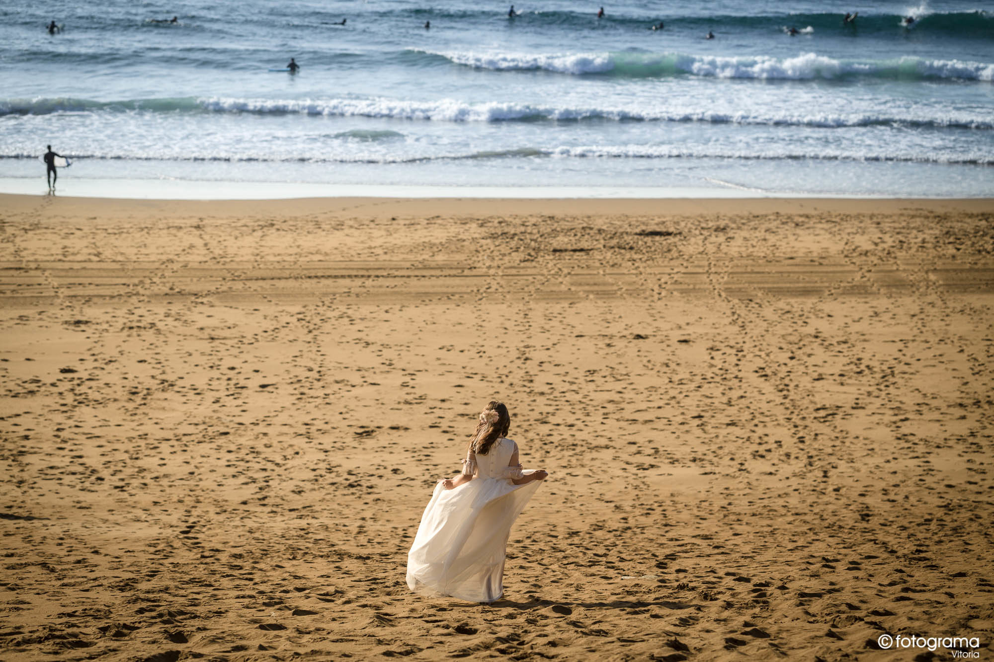 niña de comunión en la playa de sopelana mira a surfistas